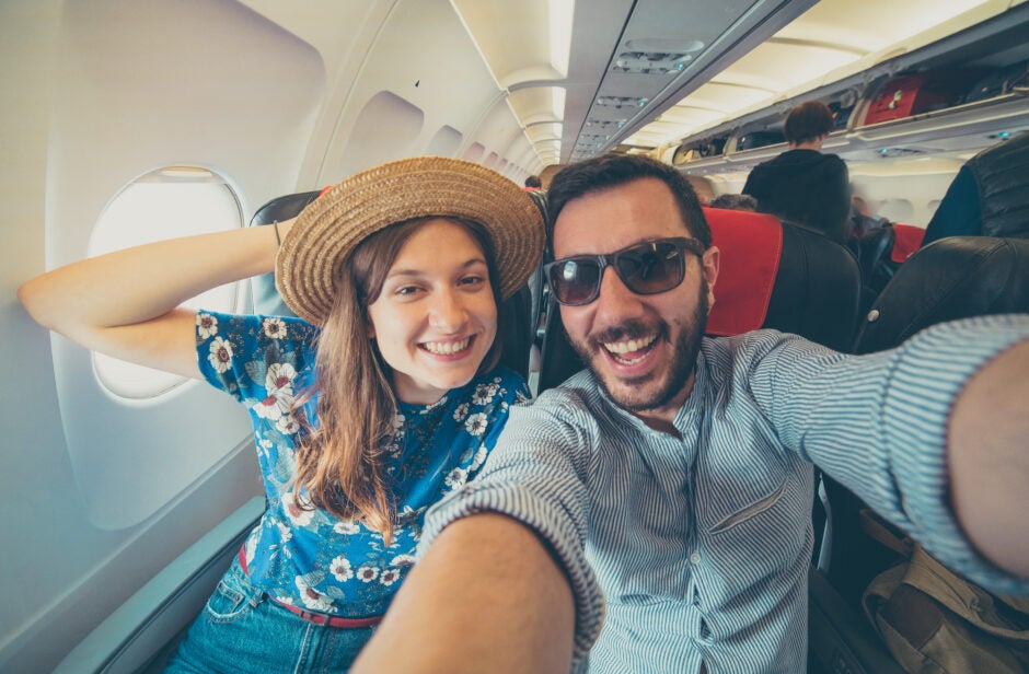 Young handsome couple taking a selfie on the airplane during flight around the world. They are a man and a woman, smiling and looking at camera. Travel, happiness and lifestyle concepts.