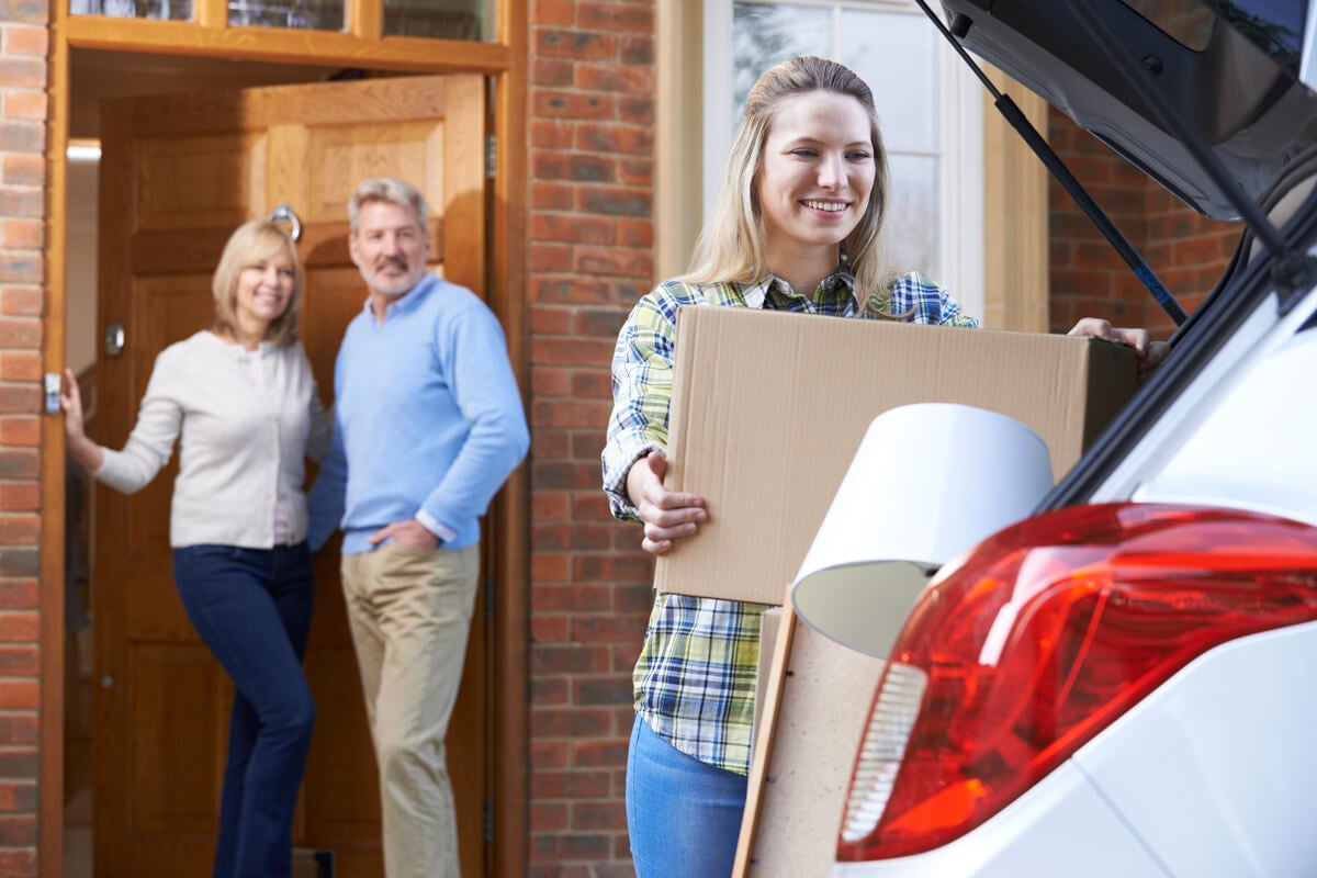 Girl packing her car while parents watch from doorway
