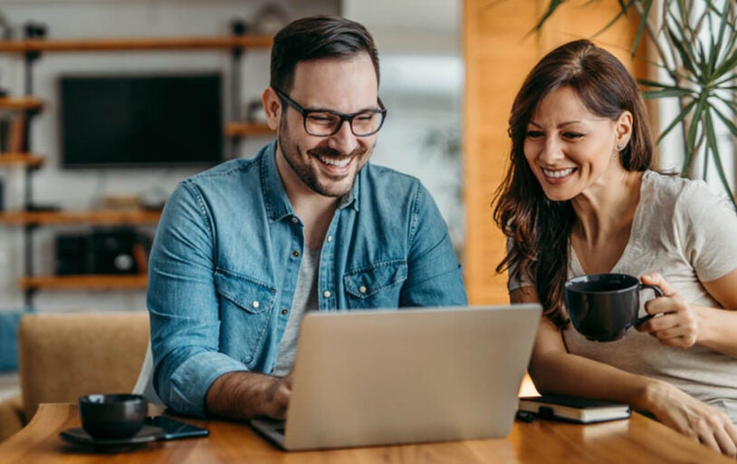 Happy couple sitting at laptop drinking coffee