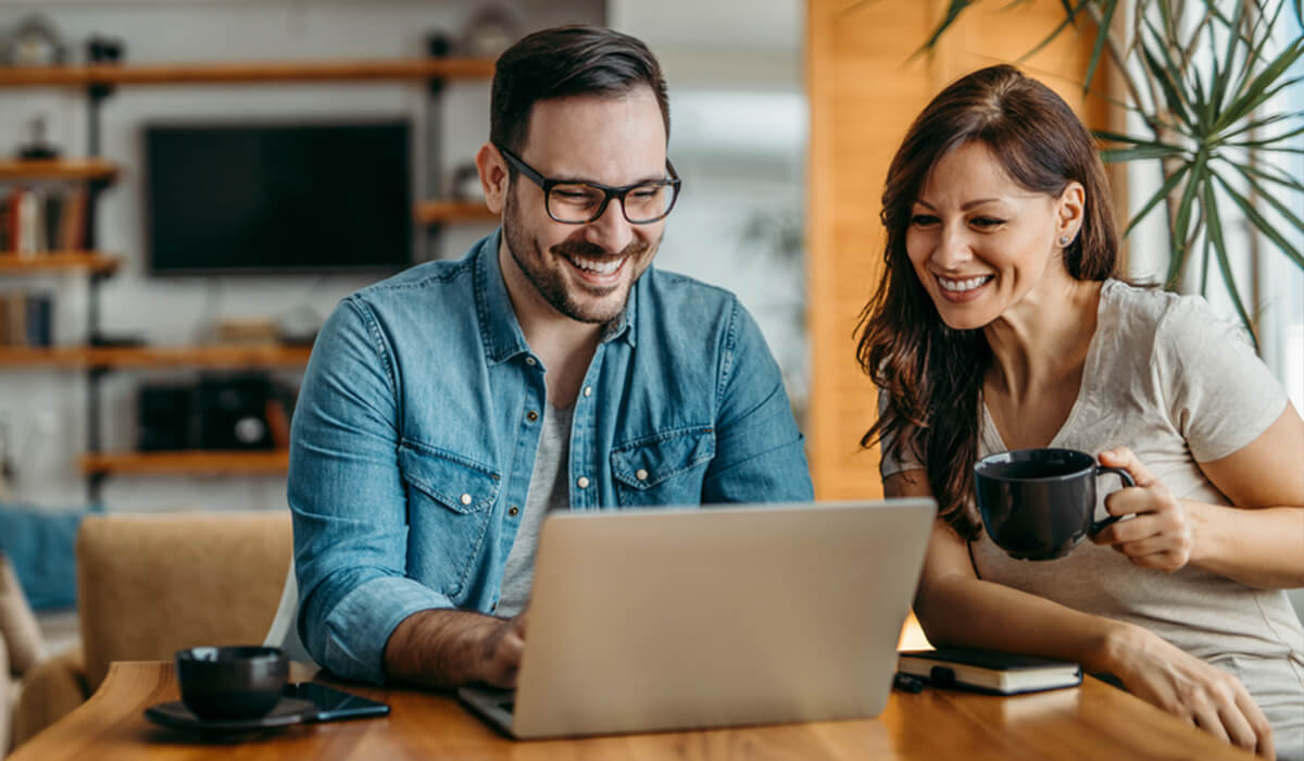 Happy couple sitting at laptop drinking coffee