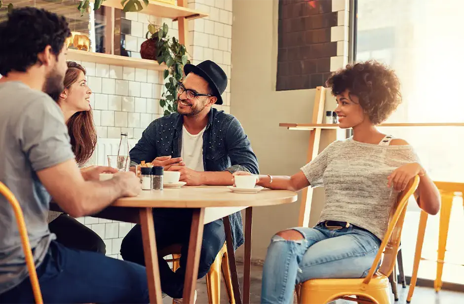 Portrait of a young group of friends meeting in a cafe. Young men and women sitting at cafe table and talking.