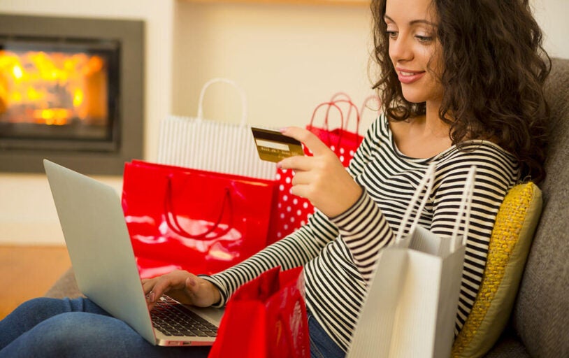 Woman sitting on couch with shopping bags and laptop holding a credit card