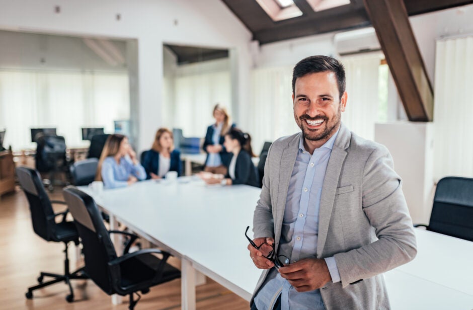 Man smiling at conference table in front of people