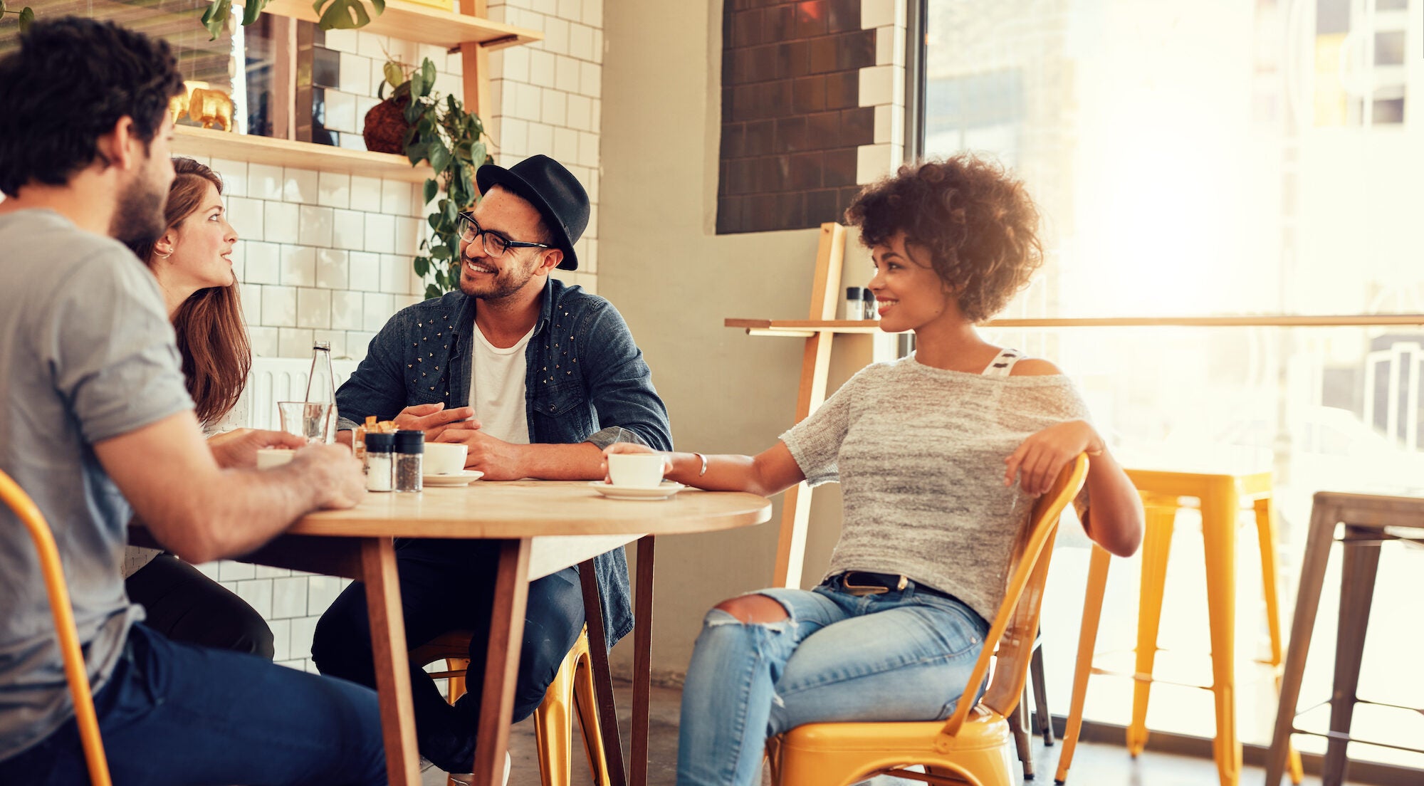 Portrait of a young group of friends meeting in a cafe. Young men and women sitting at cafe table and talking.