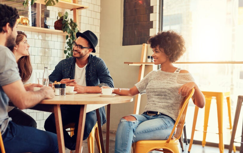 Portrait of a young group of friends meeting in a cafe. Young men and women sitting at cafe table and talking.