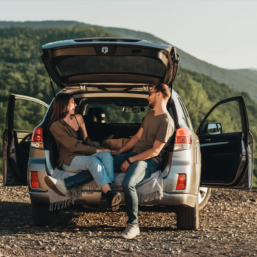 Couple sitting in back hatch of vehicle.