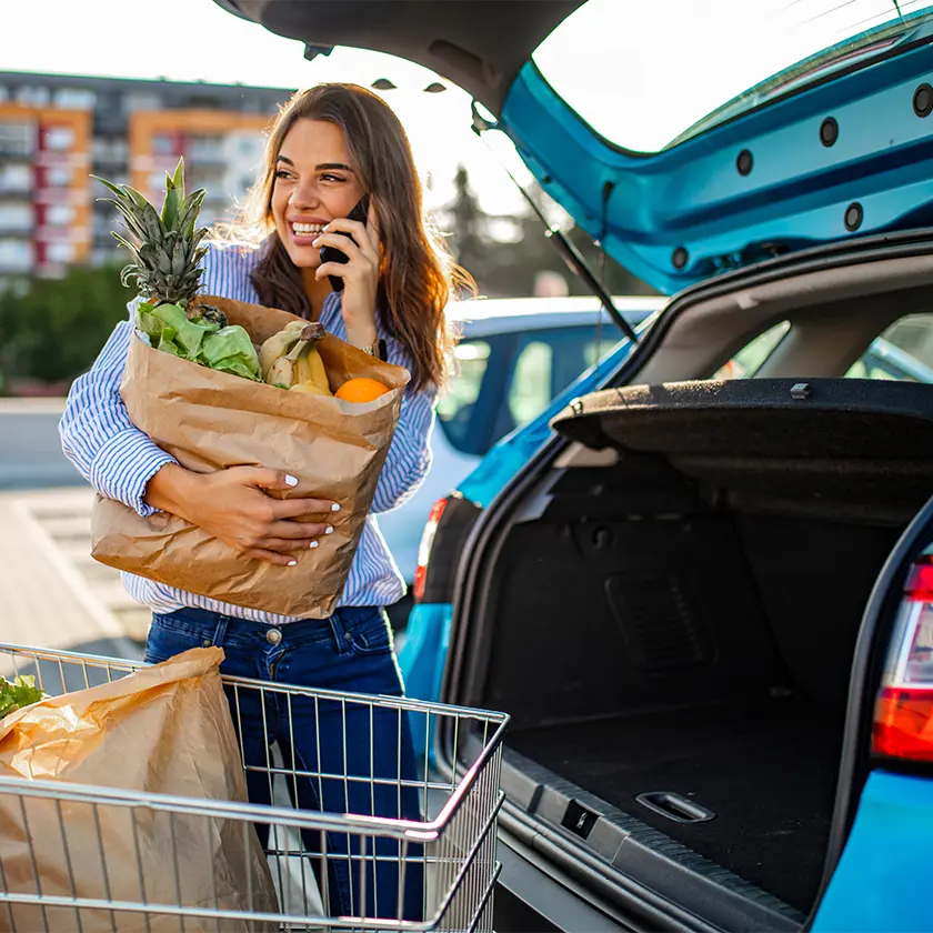 Woman loading groceries into car while talking on the phone.